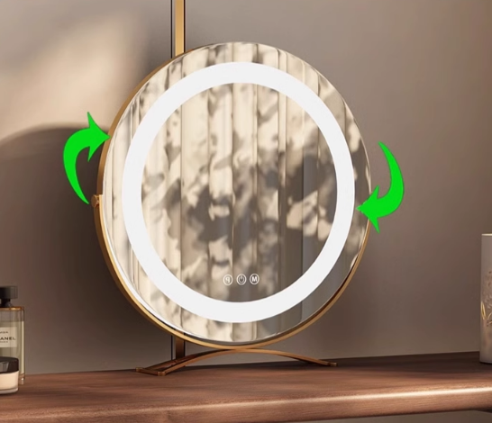 Round illuminated mirror with gold frame on a wooden surface, with green arrows indicating rotation.