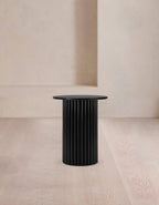 Black cylindrical side table against a beige wall