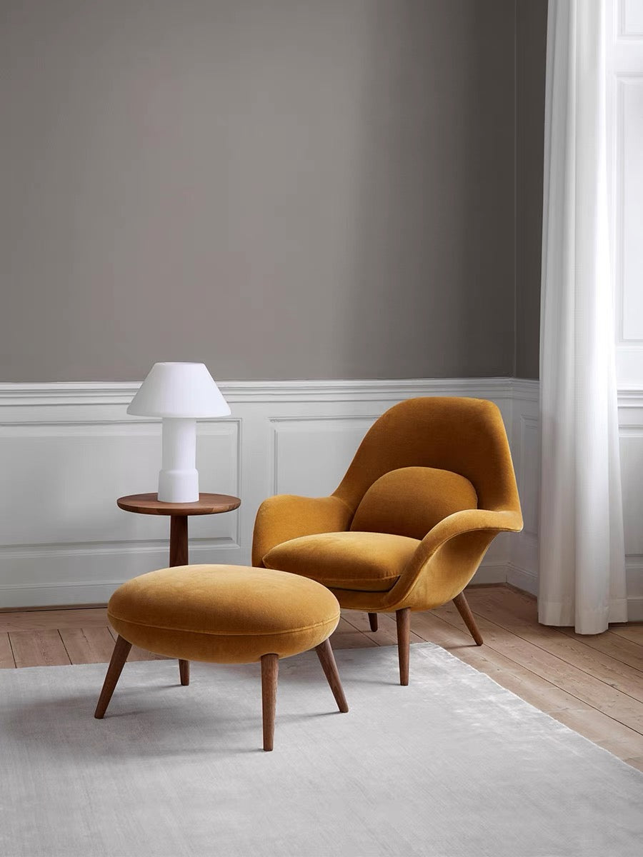 Mustard yellow armchair and ottoman with a white lamp on a wooden side table against a gray wall.