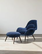 Blue velvet armchair with matching ottoman on a neutral background