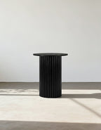 Black cylindrical side table against a white wall