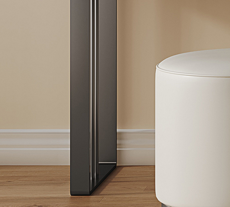 Black refrigerator against a beige wall with a white ottoman on a wooden floor.