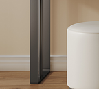 Black refrigerator against a beige wall with a white ottoman on a wooden floor.