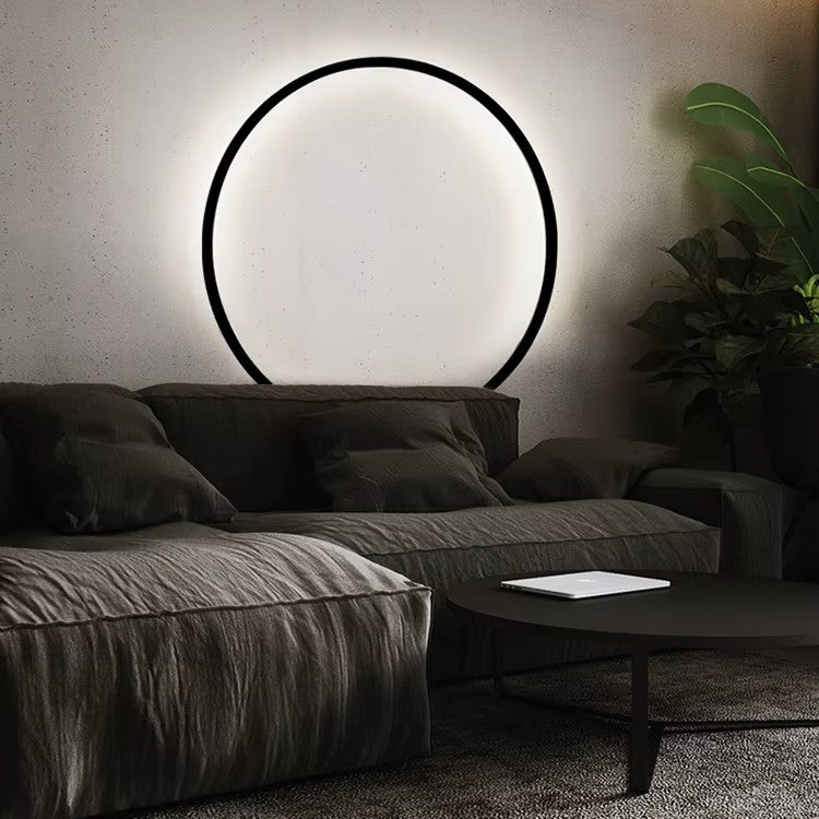 Modern living room with a dark gray sectional sofa, round coffee table, and circular wall light fixture.
