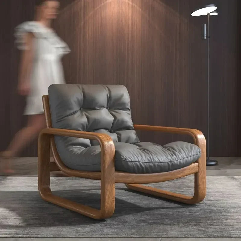Gray cushioned armchair with wooden frame in a room with a blurred person and lamp in the background.