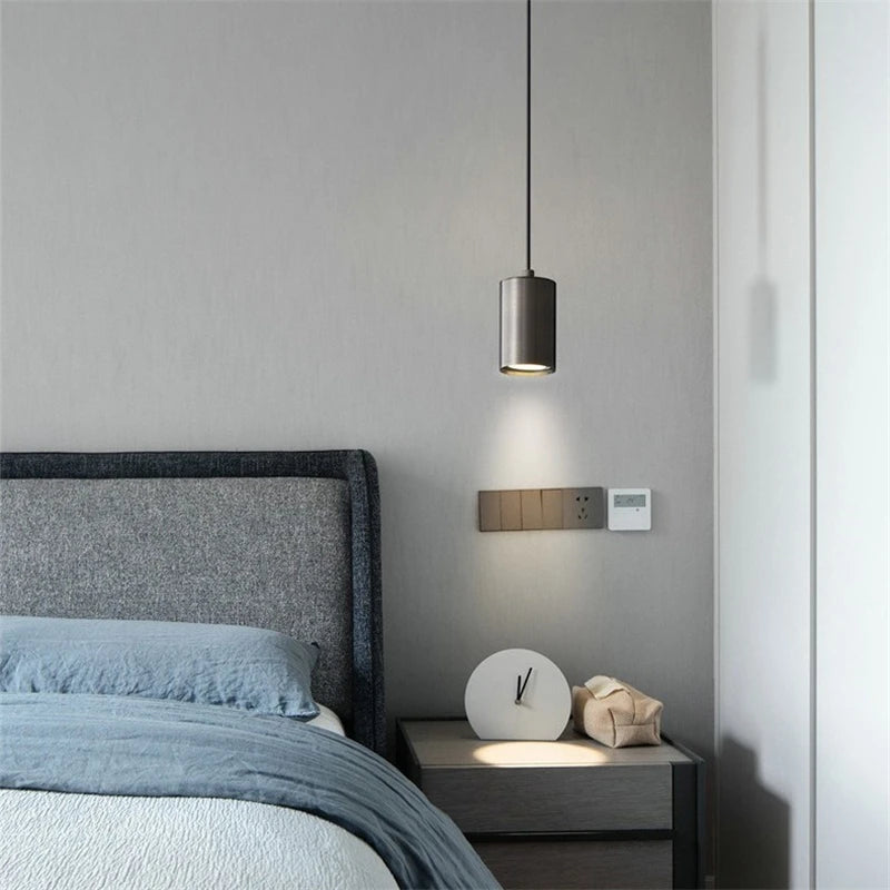 Modern bedroom with gray bed, pendant light, and nightstand with clock.