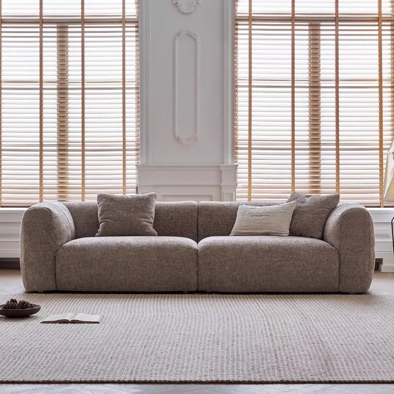 Gray sofa with cushions in a room with wooden blinds and a decorative wall.
