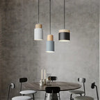 Modern pendant lights hanging above a dining table with chairs against a concrete wall.
