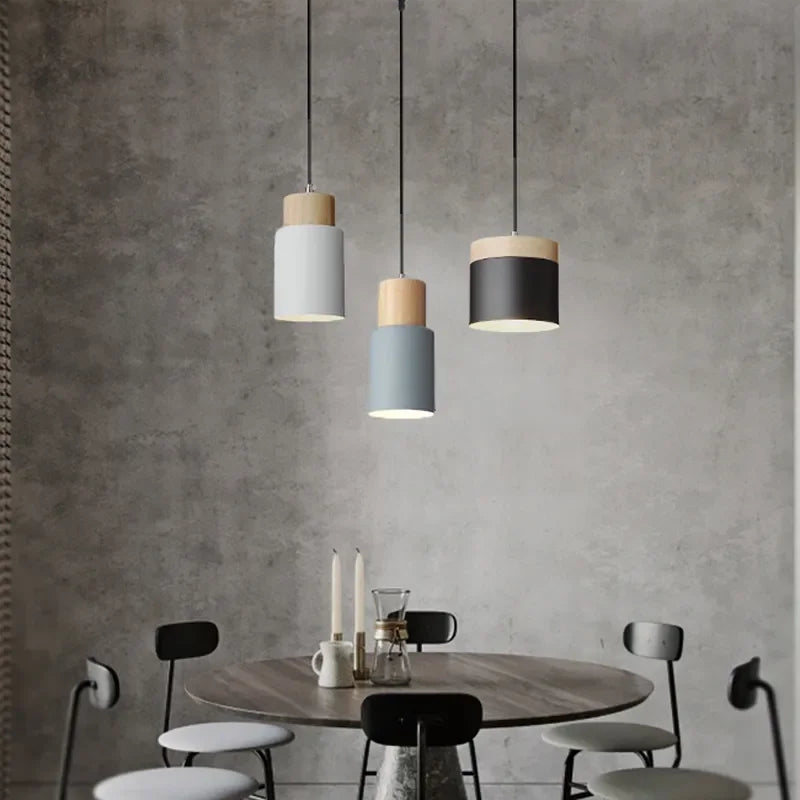 Modern pendant lights hanging above a dining table with chairs against a concrete wall.