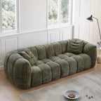 Green sofa in a room with large windows and a lamp.