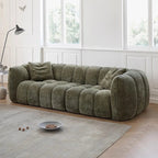 Green sofa in a room with large windows and a rug.