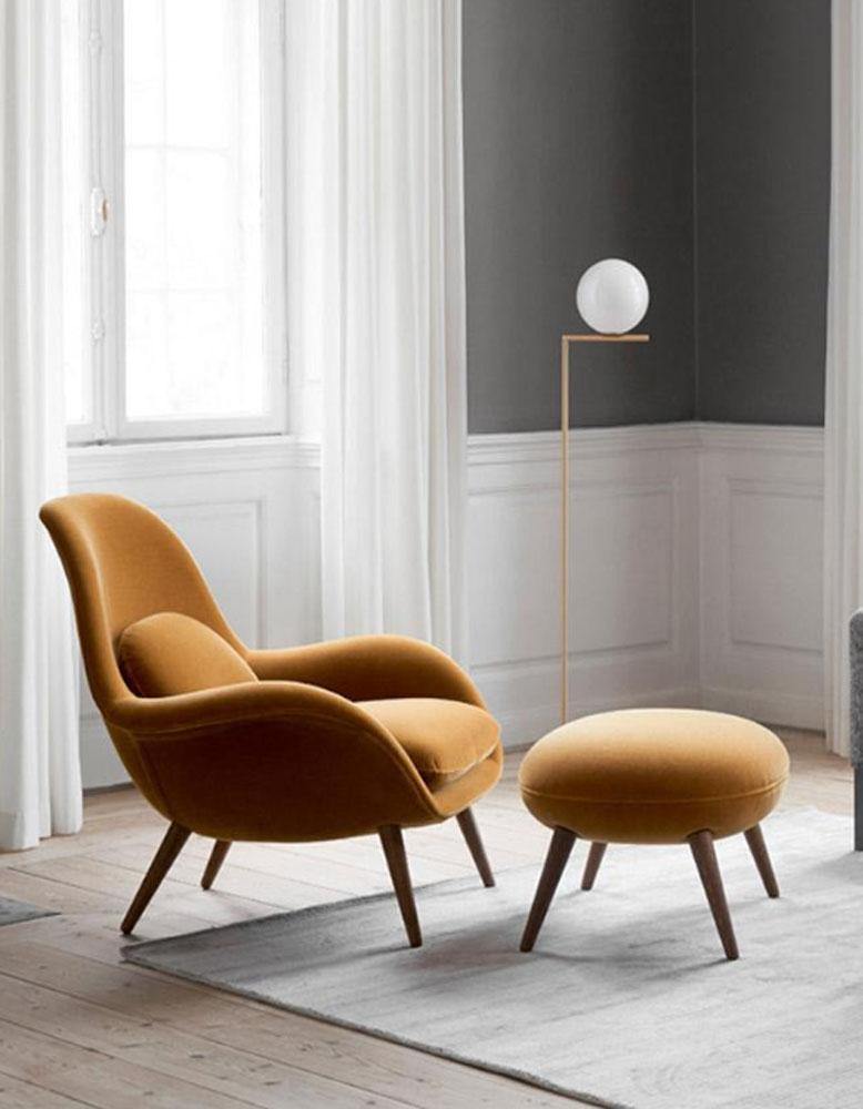 Mustard yellow armchair and ottoman with a floor lamp in a room with large windows and white curtains.