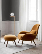 Brown armchair and ottoman in a room with a lamp and window.