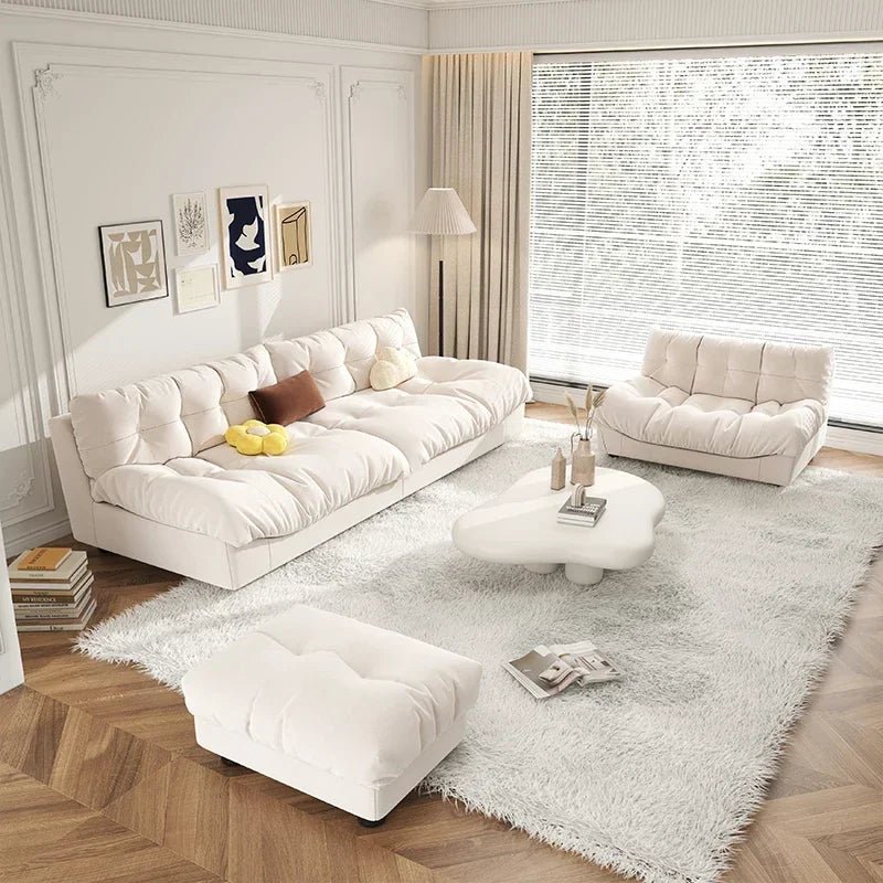 Modern living room with white sofa, ottoman, and coffee table on a light gray rug.