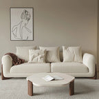 Beige sofa with cushions in a living room setting, featuring a coffee table and wall art.