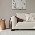 Beige sofa with a brown blanket and white pillows in a living room setting.
