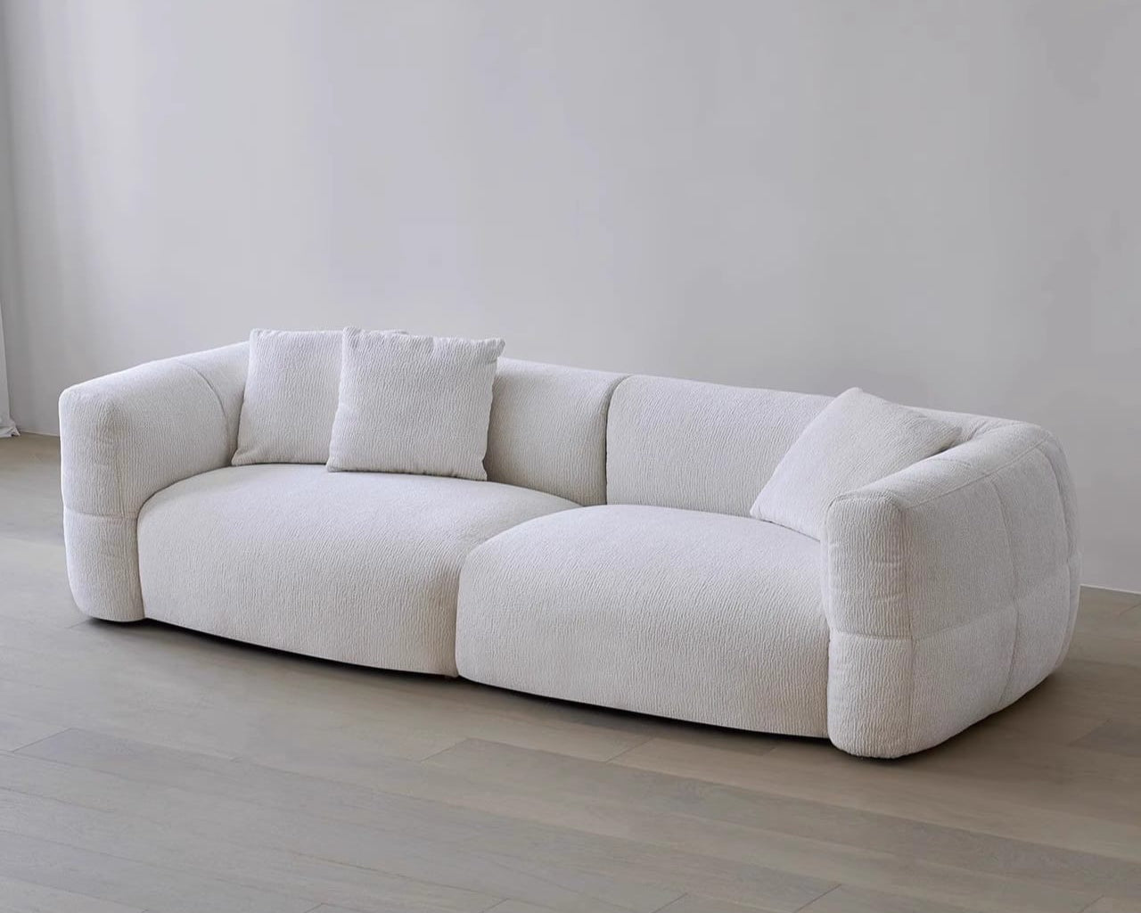 White sofa with cushions on a light wooden floor and white wall background