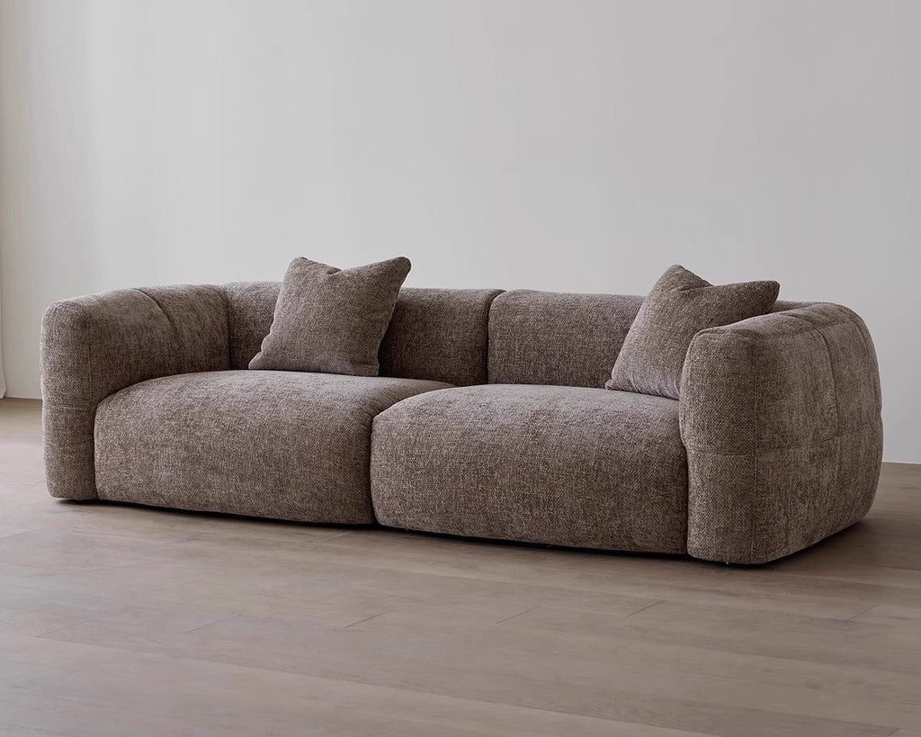 Brown sofa with two cushions on a wooden floor against a white wall