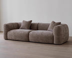 Brown sofa with two cushions on a wooden floor against a white wall